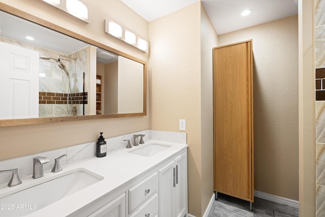 full bathroom featuring double vanity, baseboards, a tile shower, and a sink