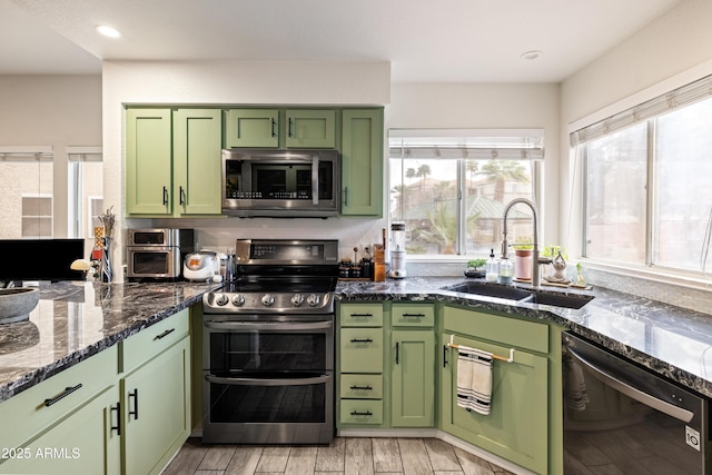 kitchen featuring green cabinetry, dark stone countertops, stainless steel appliances, light wood-type flooring, and a sink