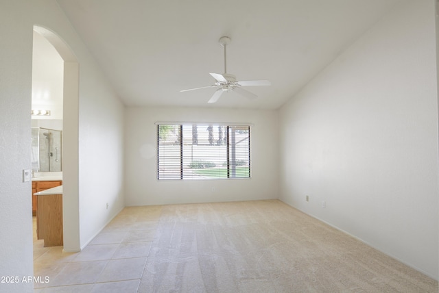 unfurnished room with lofted ceiling, arched walkways, a ceiling fan, and light colored carpet