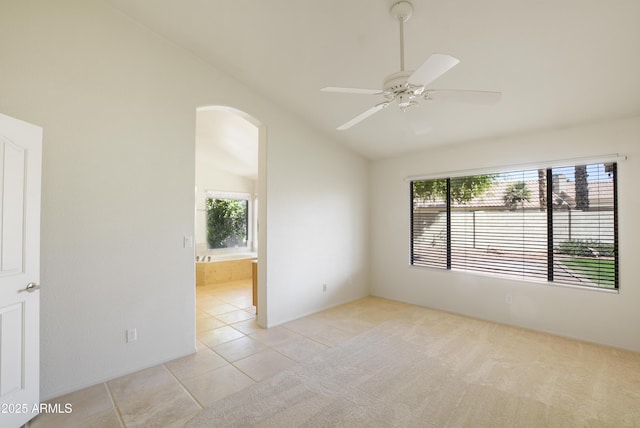 unfurnished room with lofted ceiling, a healthy amount of sunlight, light carpet, and arched walkways