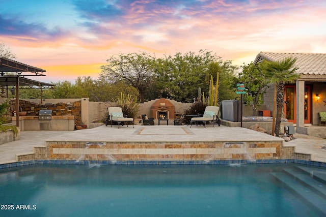 26475 N Wrangler Rd, Scottsdale, AZ 85255 - pool at dusk featuring a lit fireplace, exterior kitchen, a patio, and an outdoor pool