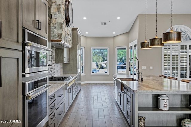 26475 N Wrangler Rd, Scottsdale, AZ 85255 - kitchen with appliances with stainless steel finishes, light stone counters, a center island with sink, dark wood finished floors, and hanging light fixtures