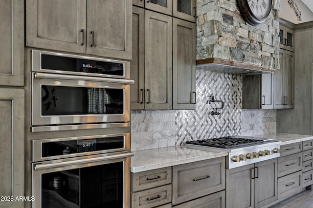 26475 N Wrangler Rd, Scottsdale, AZ 85255 - kitchen featuring stainless steel appliances, ventilation hood, backsplash, light stone counters, and glass insert cabinets
