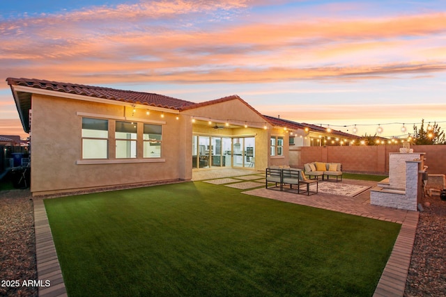 back house at dusk with ceiling fan, a yard, an outdoor living space with a fireplace, and a patio area