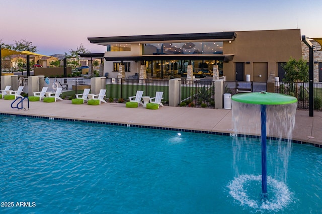 pool at dusk with pool water feature and a patio area