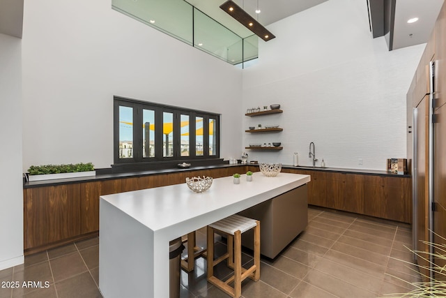 kitchen featuring a kitchen island, a towering ceiling, a breakfast bar, sink, and tile patterned floors