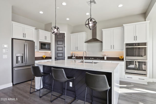 kitchen featuring sink, appliances with stainless steel finishes, an island with sink, white cabinets, and decorative light fixtures