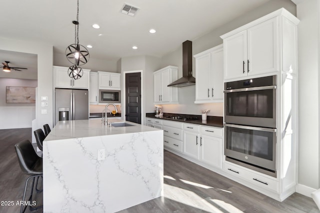 kitchen featuring sink, a kitchen breakfast bar, wall chimney range hood, a kitchen island with sink, and black appliances