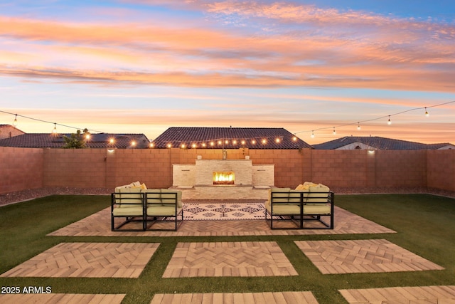 patio terrace at dusk featuring exterior fireplace and a yard