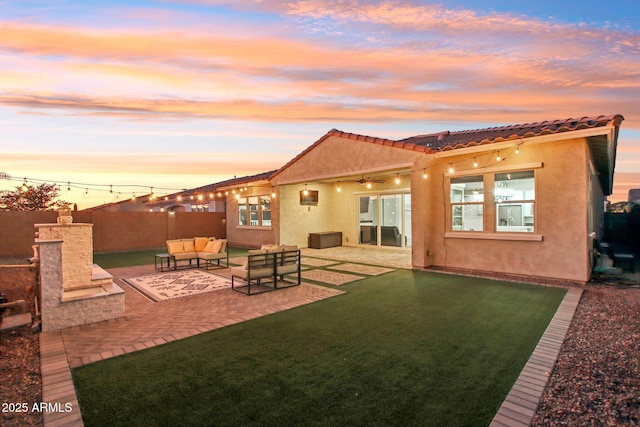 back house at dusk featuring a yard, an outdoor living space with a fireplace, and a patio