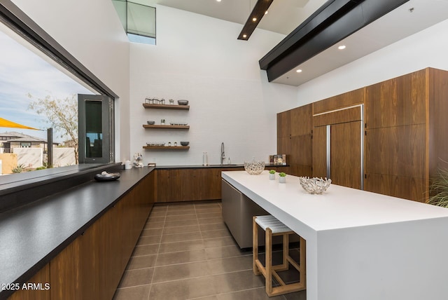 kitchen with a towering ceiling, sink, a breakfast bar area, dark tile patterned flooring, and paneled refrigerator