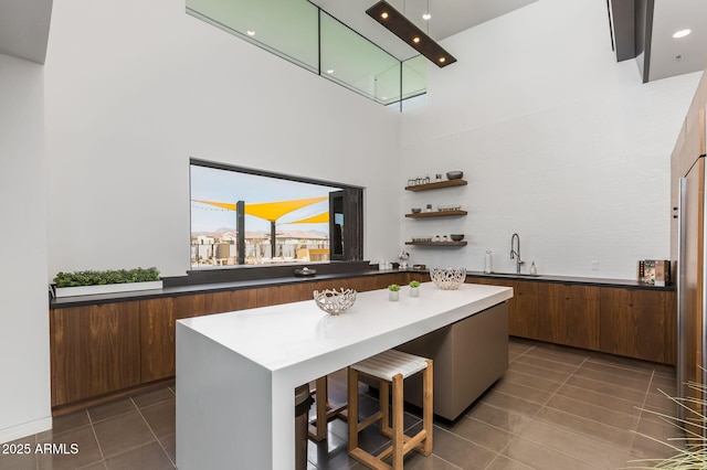 kitchen with a towering ceiling, sink, dark tile patterned flooring, a kitchen breakfast bar, and a center island