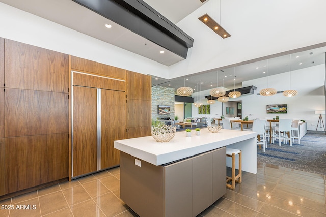 kitchen featuring a spacious island, a kitchen bar, light tile patterned floors, paneled built in refrigerator, and a towering ceiling