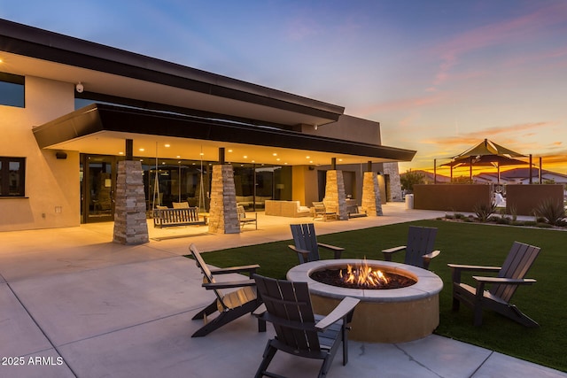 patio terrace at dusk featuring a lawn and an outdoor living space with a fire pit