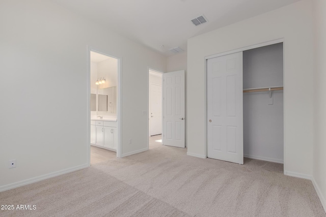 unfurnished bedroom with light carpet, a closet, and ensuite bath