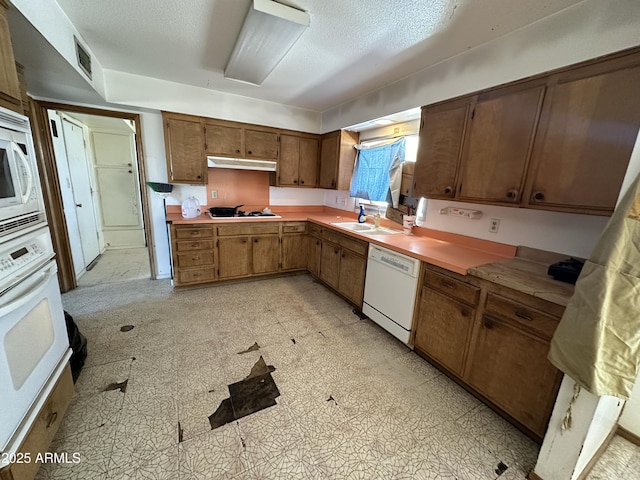 kitchen featuring under cabinet range hood, white appliances, a sink, light floors, and brown cabinetry