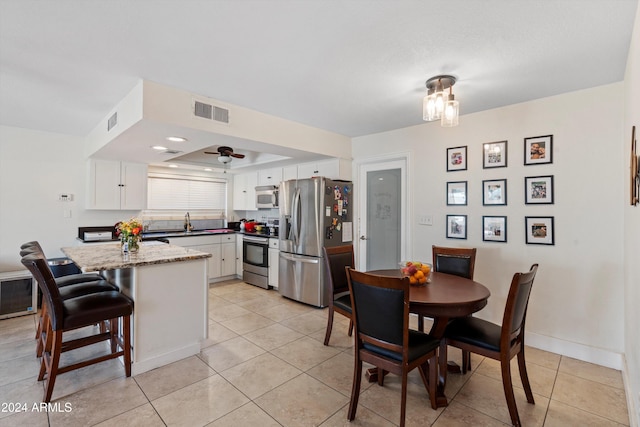 kitchen featuring white cabinetry, sink, stainless steel appliances, light stone counters, and a breakfast bar