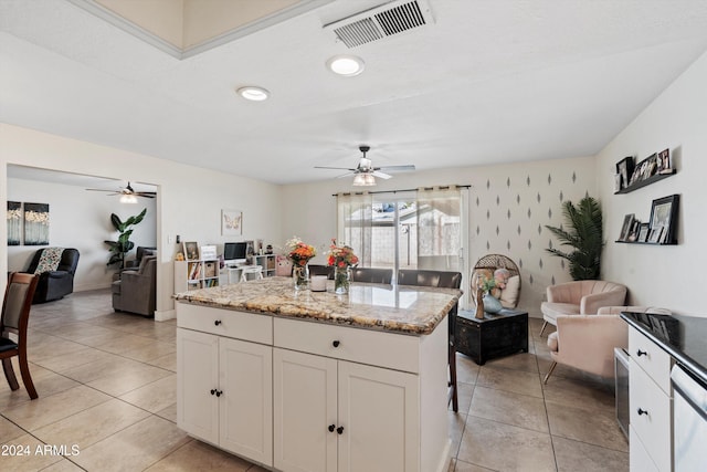 kitchen featuring dishwasher, a center island, white cabinets, light stone countertops, and light tile patterned floors