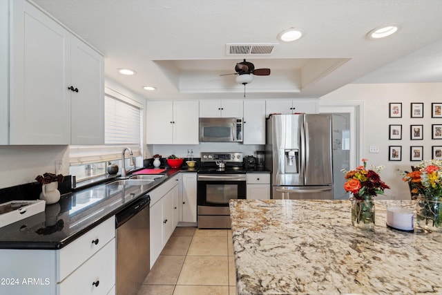 kitchen with stainless steel appliances, a tray ceiling, ceiling fan, sink, and white cabinetry