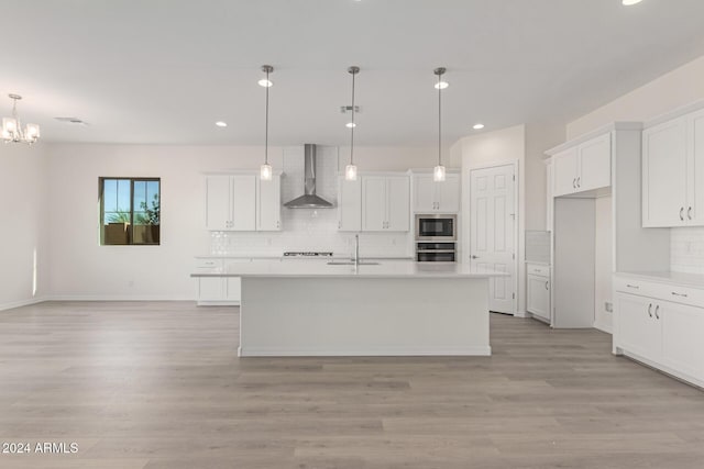 kitchen with wall chimney exhaust hood, hanging light fixtures, an island with sink, and appliances with stainless steel finishes