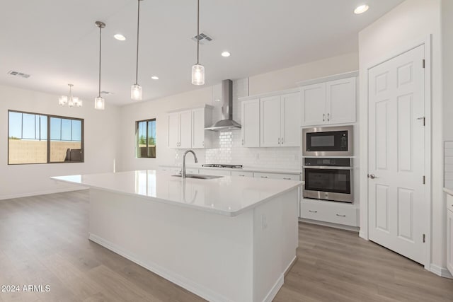 kitchen featuring sink, stainless steel appliances, a kitchen island with sink, and wall chimney range hood