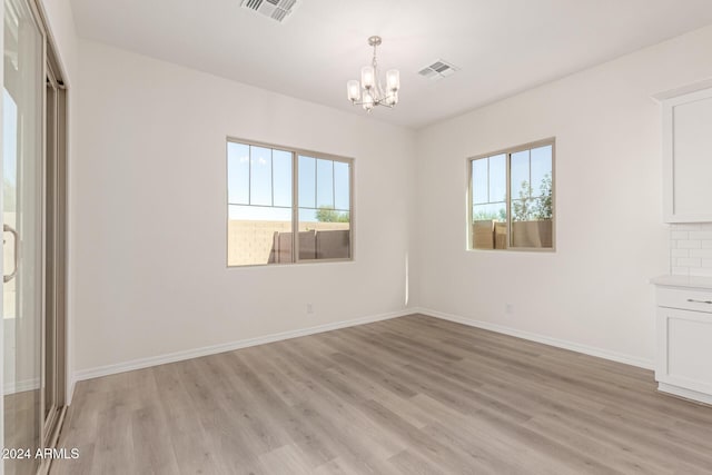 spare room with a notable chandelier and light hardwood / wood-style flooring