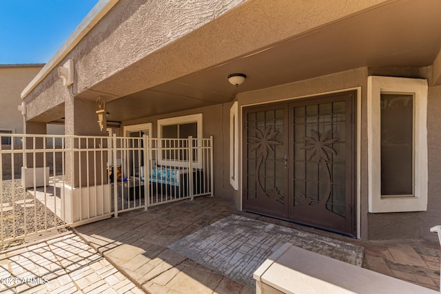 view of exterior entry with a patio area, fence, and stucco siding