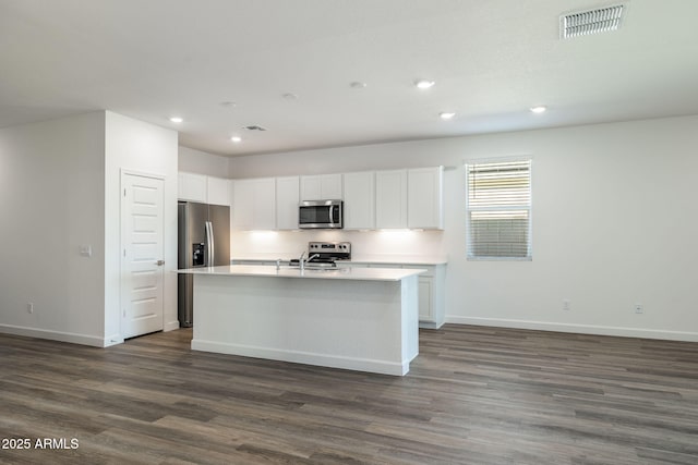 kitchen featuring appliances with stainless steel finishes, white cabinetry, dark wood finished floors, and an island with sink