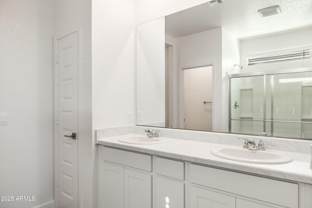 full bath with double vanity, a stall shower, a sink, and visible vents