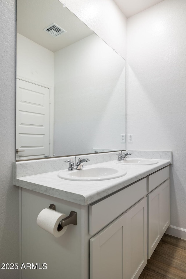 bathroom featuring double vanity, wood finished floors, a sink, and visible vents