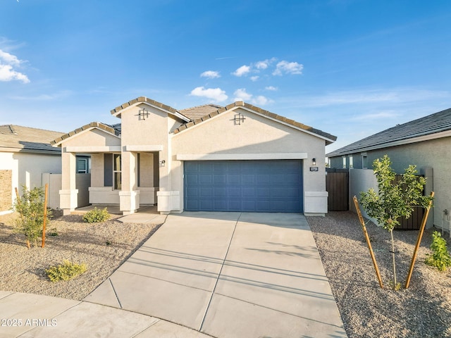 mediterranean / spanish house featuring an attached garage, fence, a tile roof, concrete driveway, and stucco siding