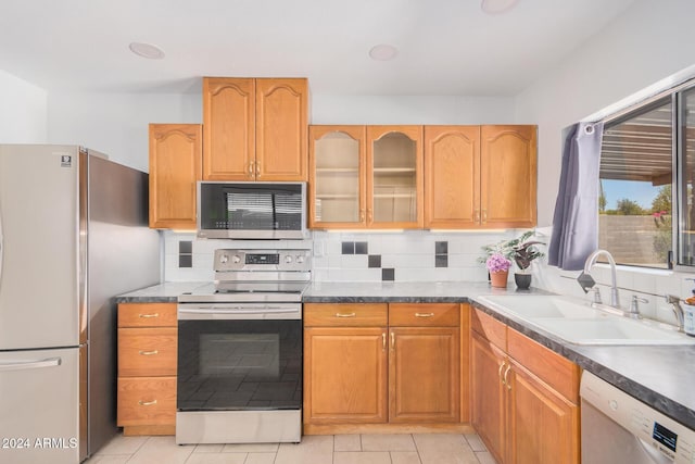 kitchen with tasteful backsplash, glass insert cabinets, appliances with stainless steel finishes, a sink, and light tile patterned flooring