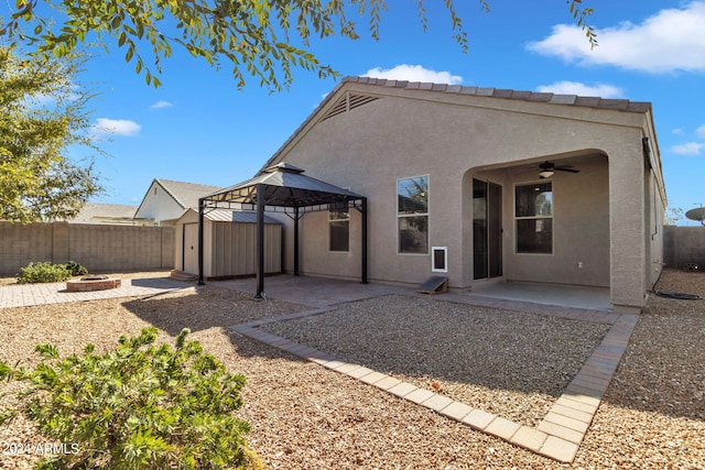 back of property with ceiling fan, an outdoor fire pit, a storage shed, a patio area, and a gazebo