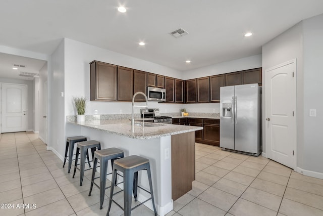 kitchen with light stone countertops, sink, kitchen peninsula, appliances with stainless steel finishes, and a kitchen bar