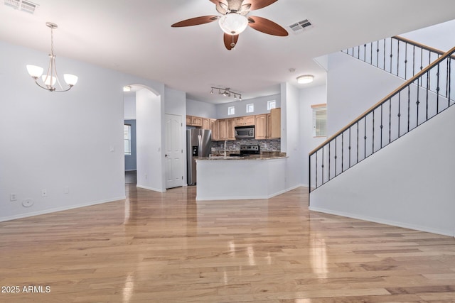 unfurnished living room with ceiling fan with notable chandelier, a wealth of natural light, rail lighting, sink, and light hardwood / wood-style floors