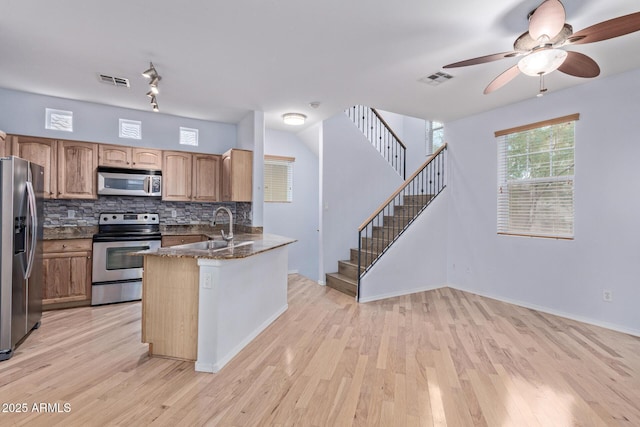 kitchen featuring sink, tasteful backsplash, dark stone countertops, appliances with stainless steel finishes, and kitchen peninsula