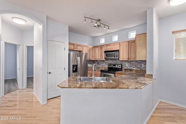 kitchen featuring sink, dark stone countertops, stainless steel appliances, decorative backsplash, and light wood-type flooring