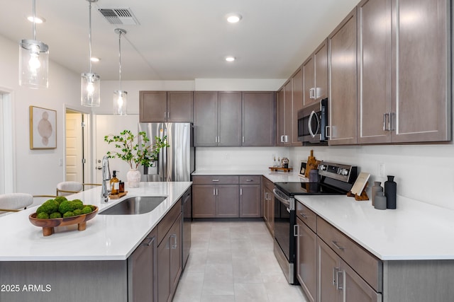kitchen featuring a sink, stainless steel appliances, light countertops, and a center island with sink