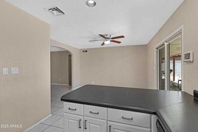 kitchen featuring ceiling fan, light tile patterned flooring, dark countertops, and arched walkways