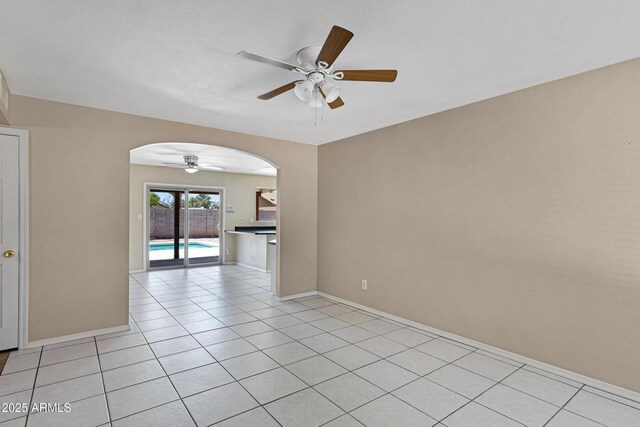 empty room with a ceiling fan, arched walkways, light tile patterned floors, and baseboards