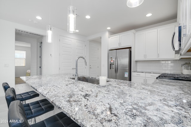 kitchen featuring appliances with stainless steel finishes, decorative backsplash, white cabinetry, a breakfast bar area, and hanging light fixtures