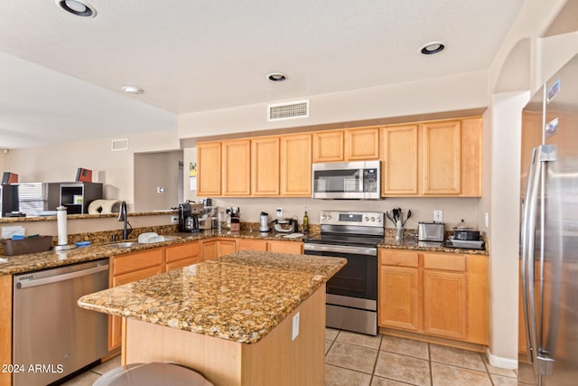 kitchen with light stone countertops, a center island, stainless steel appliances, sink, and light tile patterned flooring