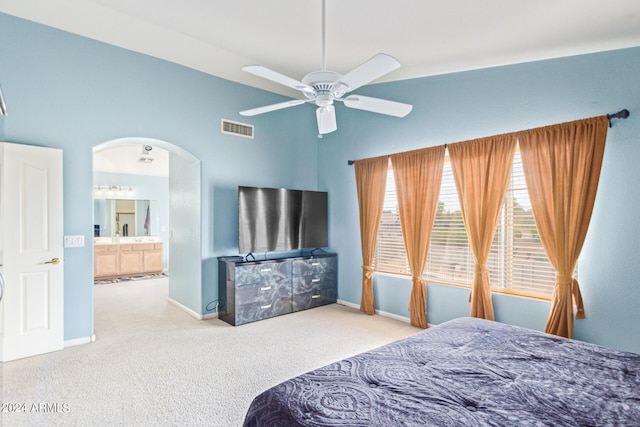 bedroom featuring ceiling fan, ensuite bath, light carpet, and a high ceiling