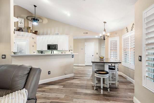 kitchen with kitchen peninsula, a breakfast bar, hardwood / wood-style flooring, white cabinets, and a chandelier