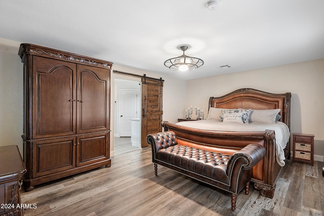 bedroom with a barn door and light hardwood / wood-style flooring