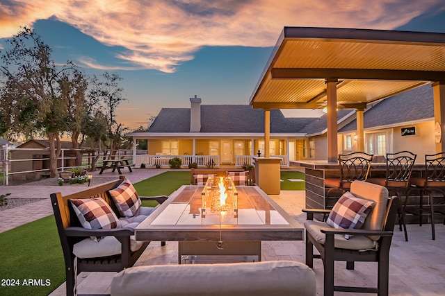 patio terrace at dusk featuring exterior bar, ceiling fan, and an outdoor living space with a fire pit