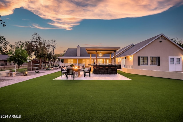 back house at dusk featuring a lawn, a patio area, an outdoor bar, and an outdoor living space with a fire pit