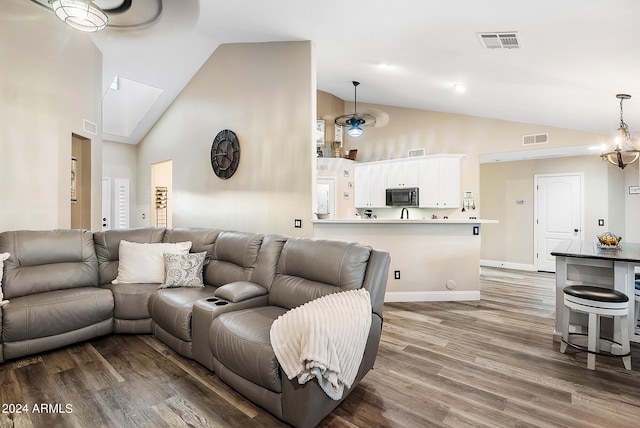 living room featuring an inviting chandelier, hardwood / wood-style flooring, high vaulted ceiling, and a skylight