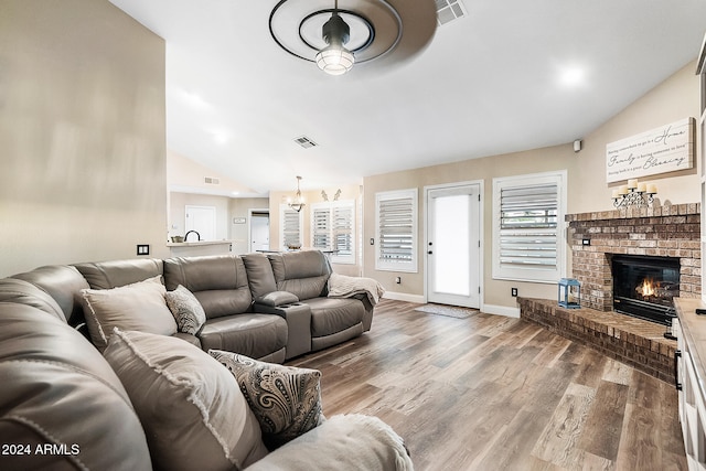 living room with hardwood / wood-style flooring, ceiling fan with notable chandelier, a fireplace, and vaulted ceiling