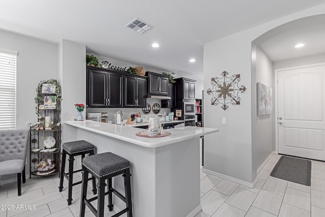 kitchen featuring visible vents, a breakfast bar, light countertops, and stainless steel microwave